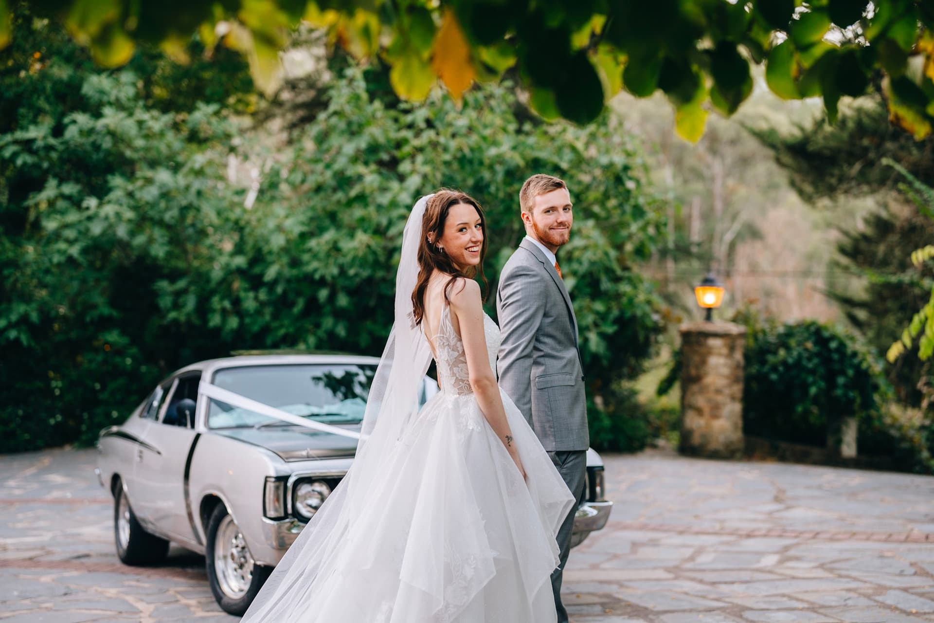 Couple beside a classic wedding car at the castle, bride looking over her shoulder