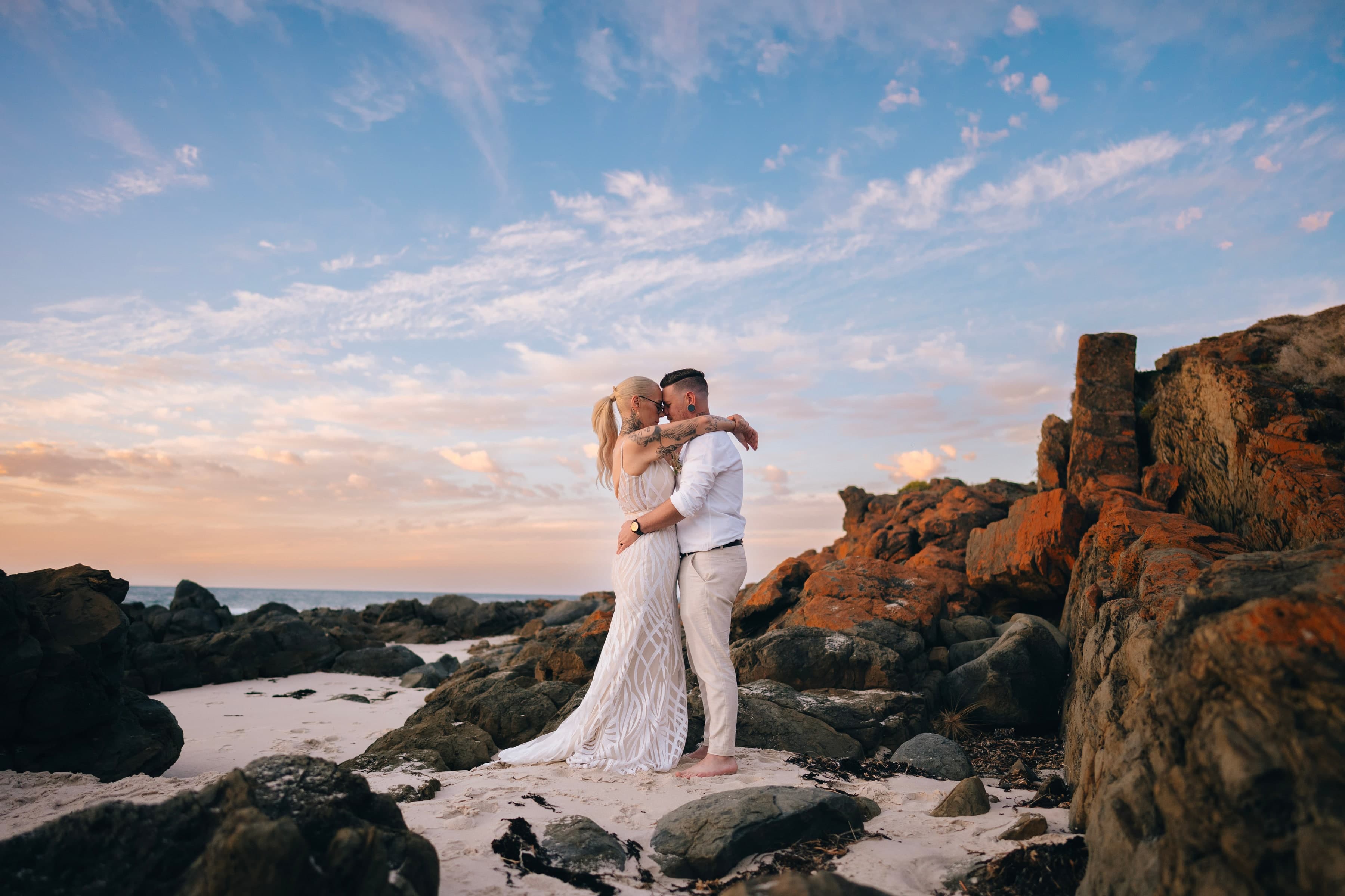 Couple embrace on coastal rocks, golden hour